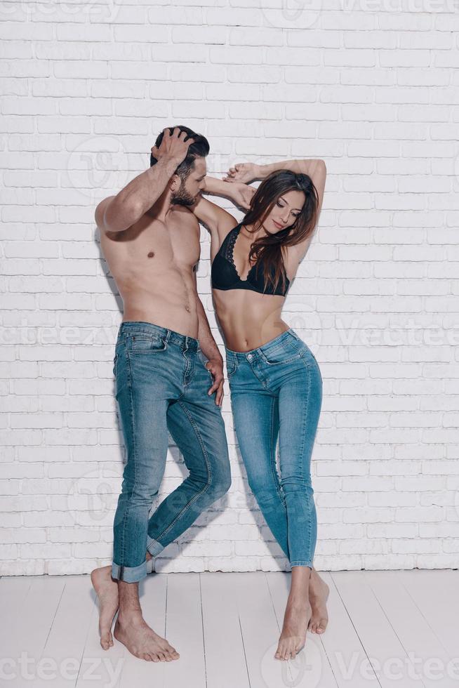 Totally in love. Full length of beautiful young couple looking away while standing against brick wall photo