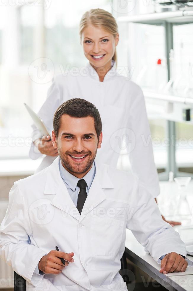 expertos médicos. dos jóvenes científicos felices mirando la cámara y sonriendo mientras trabajan juntos en el laboratorio foto