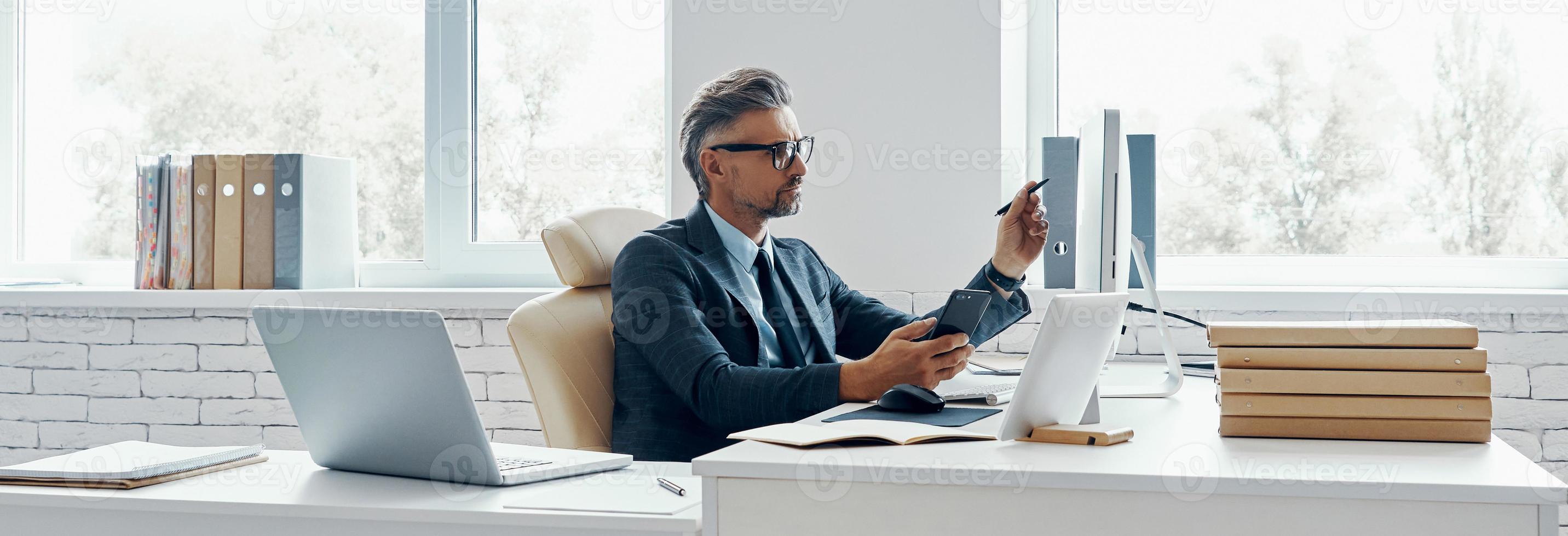 Confident mature man in formal business wear using computer while sitting in office photo