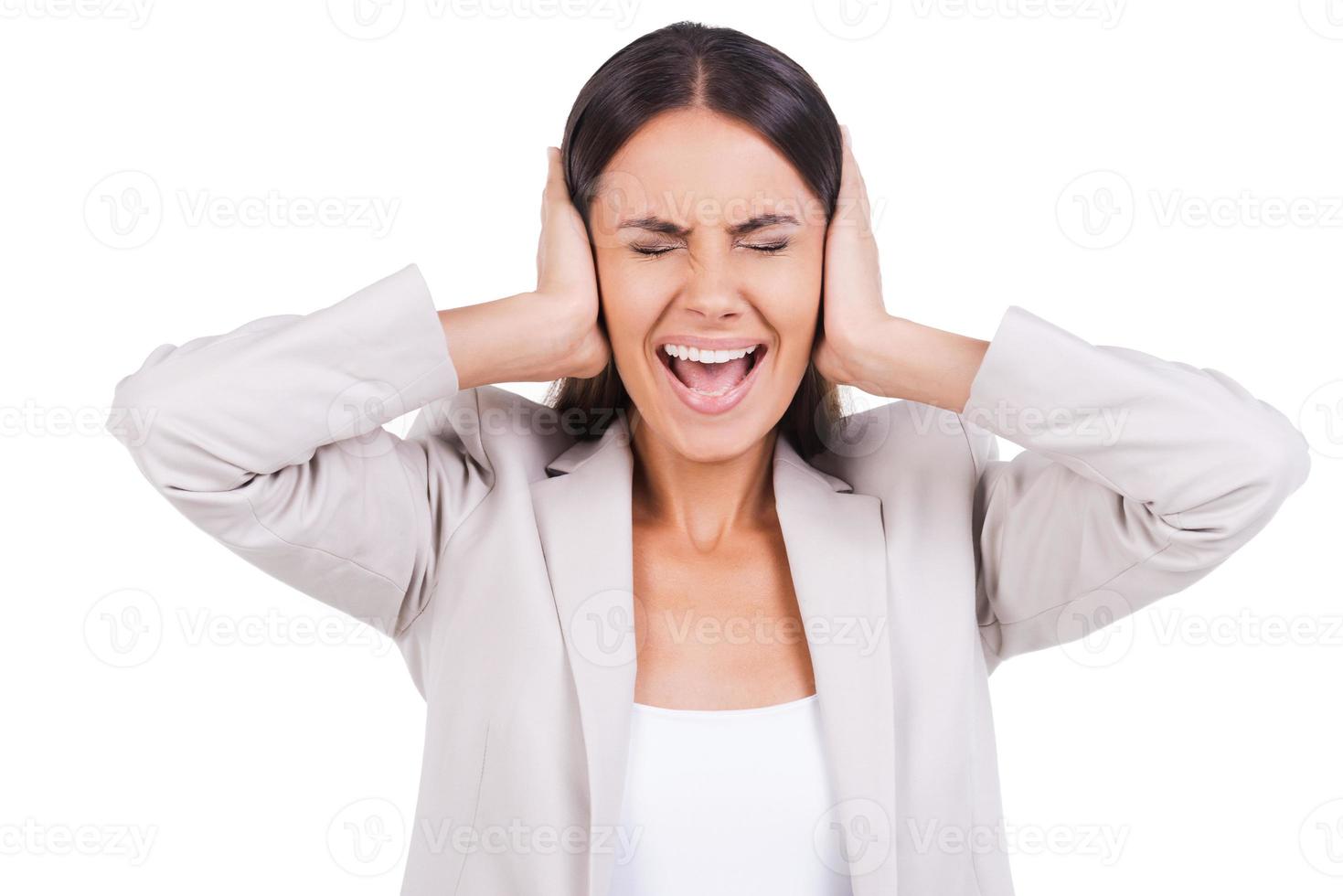 Too loud sound. Frustrated young woman covering ears with hands and keeping eyes closed while standing against white background photo