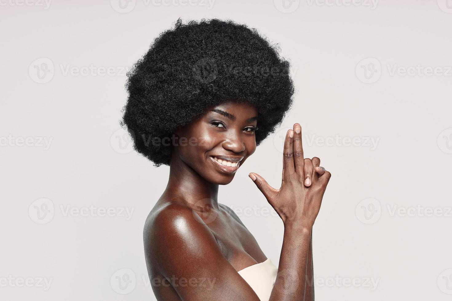 Portrait of beautiful young African woman looking at camera and gesturing while standing against gray background photo