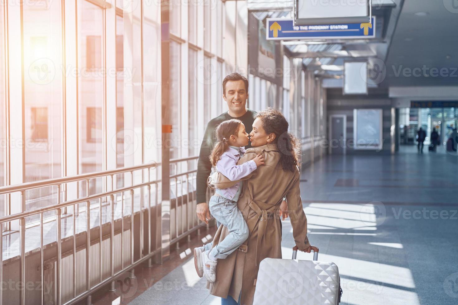 Happy father with little girl meeting wife at the airport terminal photo