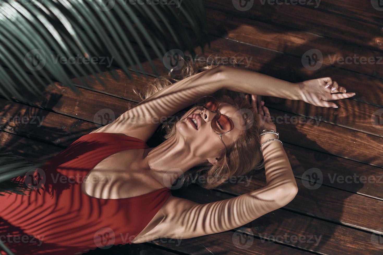 Total relaxation. Top view of beautiful young woman in swimwear keeping eyes closed and mouth open while lying under the palm tree photo