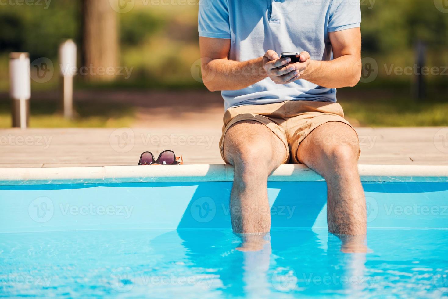 Chatting with friends. Cropped image of man sitting poolside and typing something on mobile phone photo