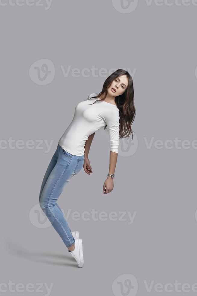 Slim and beautiful. Full length of attractive young woman in casual wear posing and looking at camera while standing against grey background photo