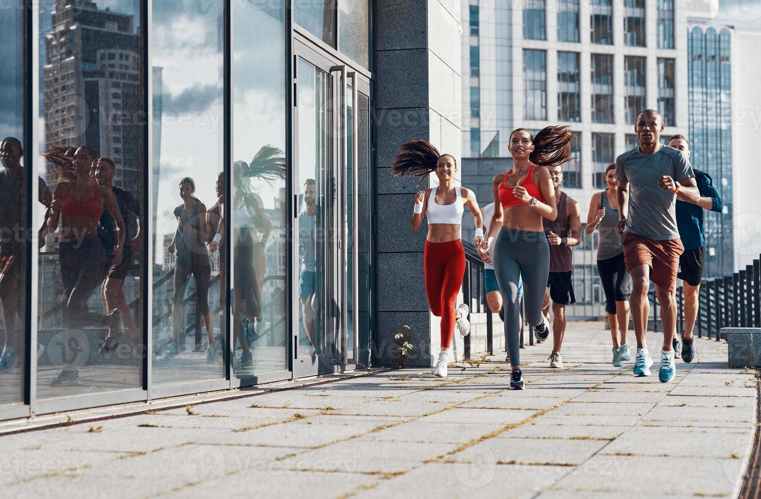 Full length of people in sports clothing jogging while exercising on the sidewalk outdoors photo