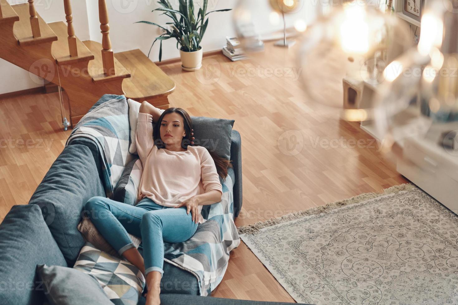 Top view of relaxed young woman in casual clothing resting on sofa while spending time at home photo