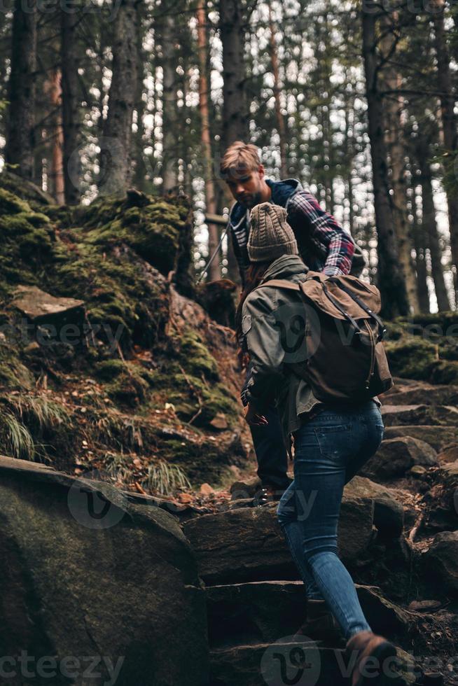 Getting in touch with nature. Young couple holding hands and moving up while hiking together in the woods photo