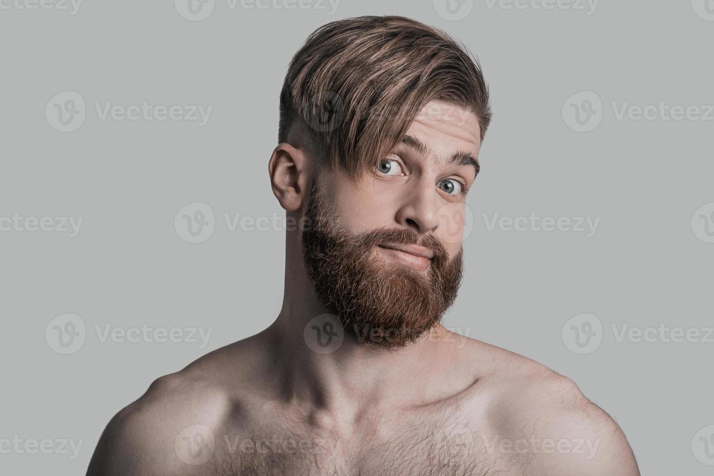 Portrait of young man looking at camera with surprised face while being in front of grey background photo