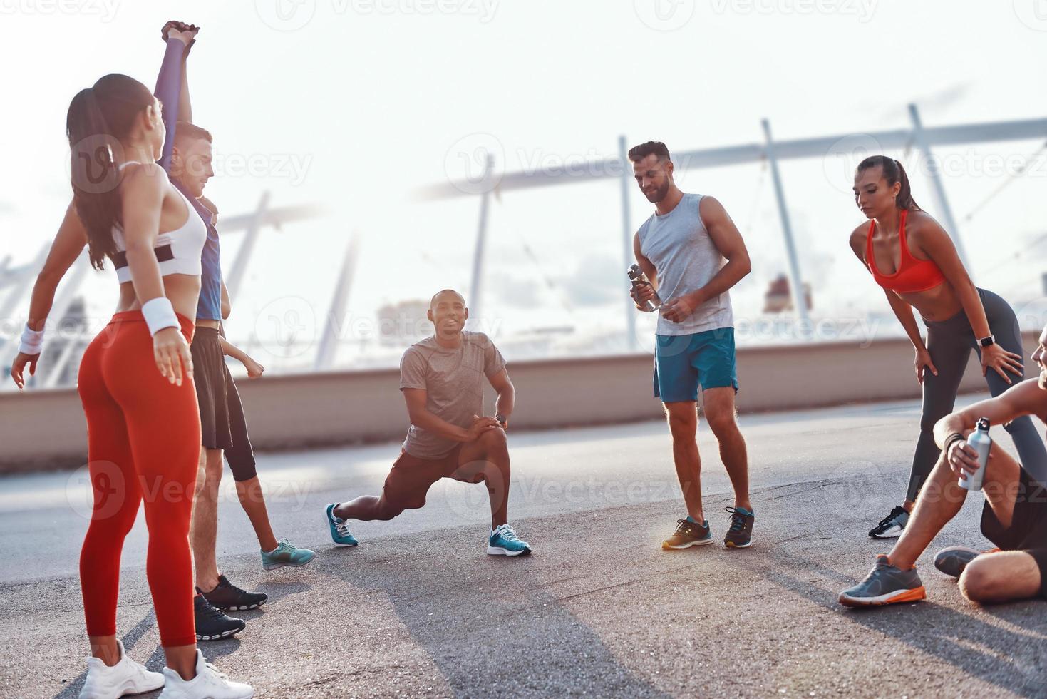 Group of people in sports clothing warming up and stretching outdoors photo