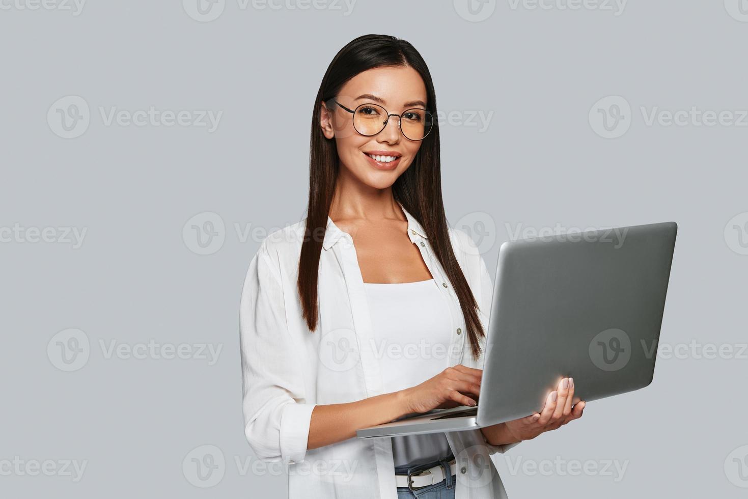 How may I help Beautiful young Asian woman looking at camera and smiling while standing against grey background photo