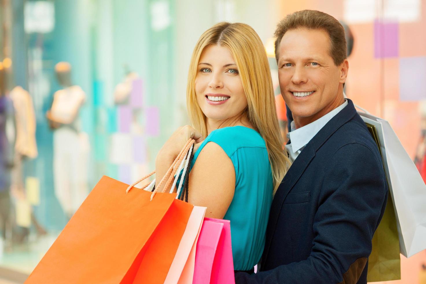 pareja de compras. alegre pareja madura sosteniendo bolsas de compras y mirando por encima del hombro mientras está de pie en el centro comercial foto