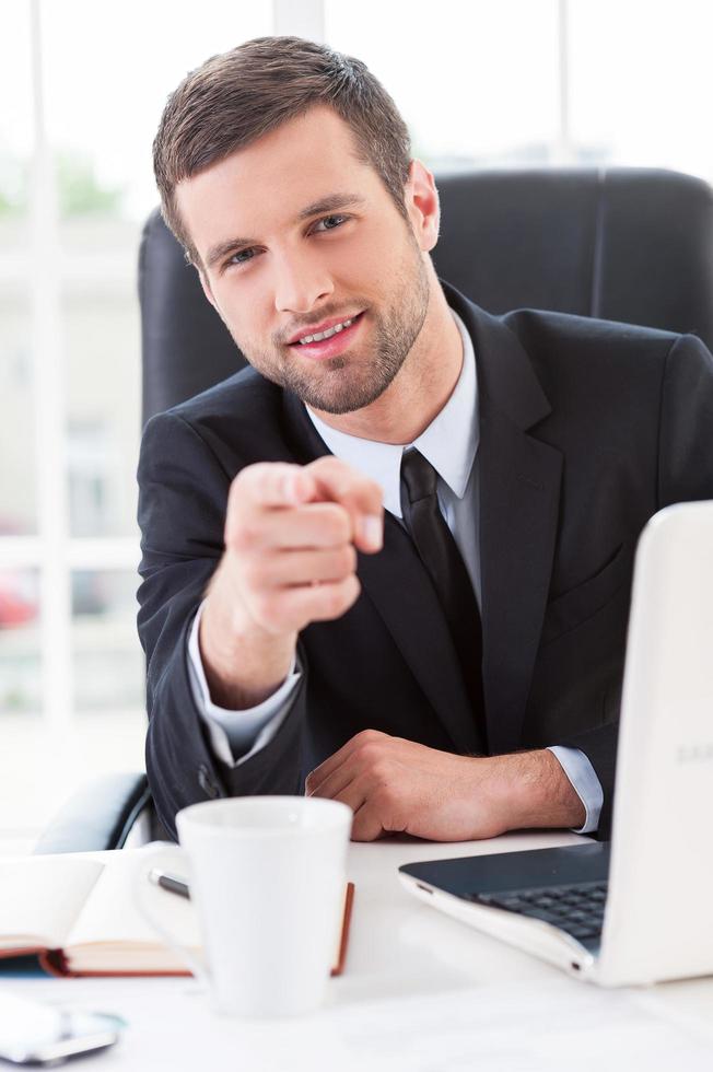 Making business easier. Confident young man in formalwear pointing you and smiling while sitting at his working place photo