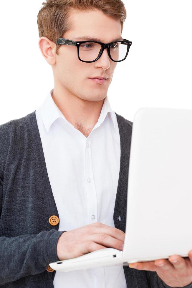 Chico IT. Apuesto joven trabajando en la computadora portátil mientras está de pie aislado en blanco foto