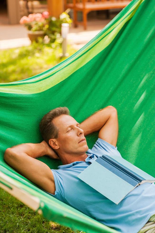 Relaxing in hammock. Happy mature man sleeping while lying in hammock with book laying on his torso photo