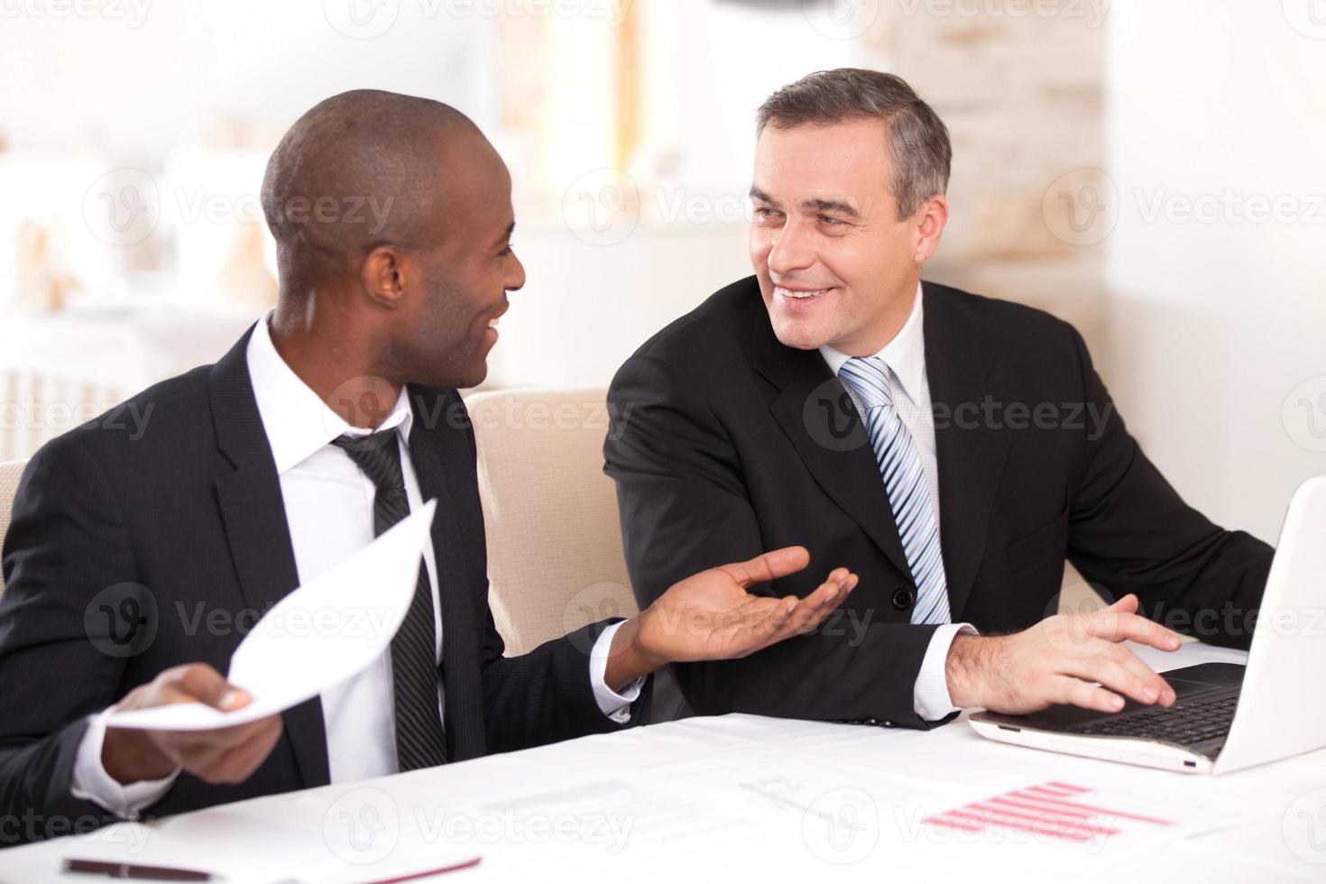 discutiendo un proyecto. dos alegres empresarios con ropa formal discutiendo algo mientras uno de ellos gesticula y sonríe foto