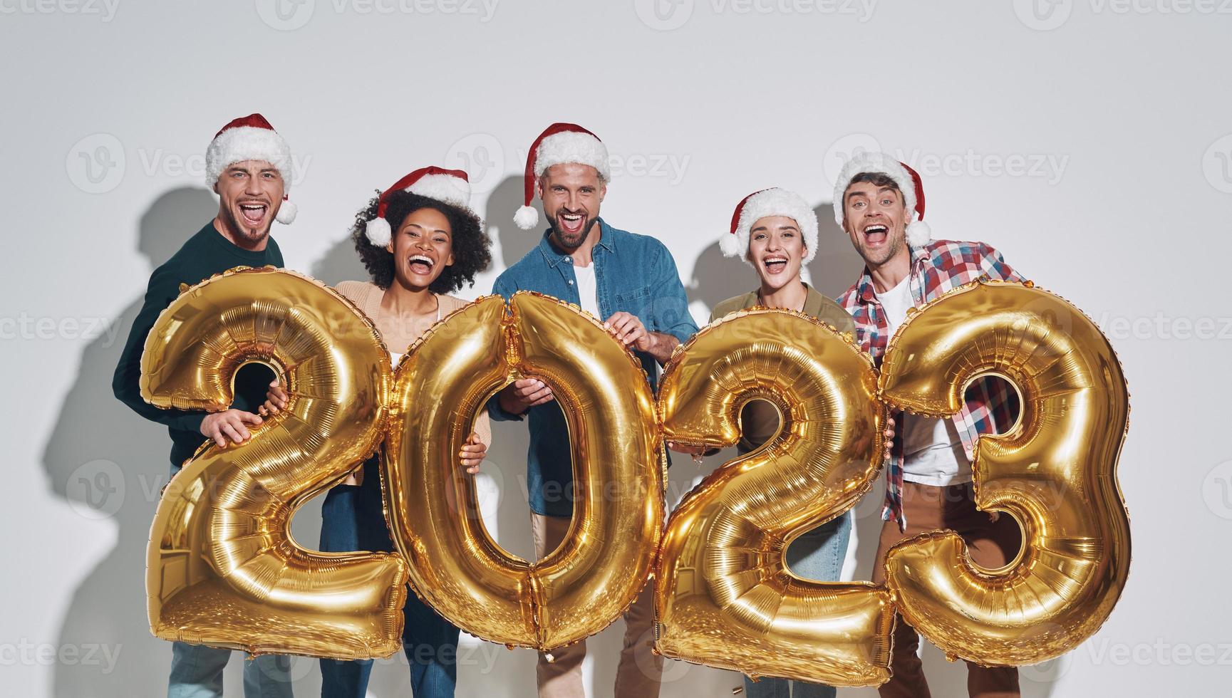 grupo de jóvenes hermosos con sombreros navideños que llevan números dorados y sonríen foto