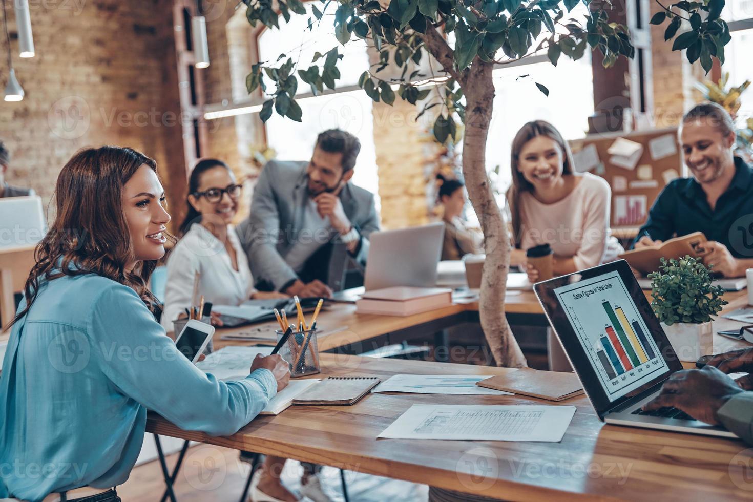 Group of young modern people in smart casual wear communicating and using modern technologies while working in the office photo