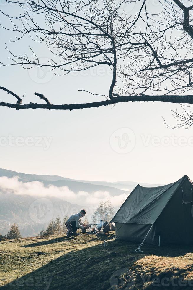 He is the fire starter. Young man making a campfire while sitting near the tent in the mountains photo