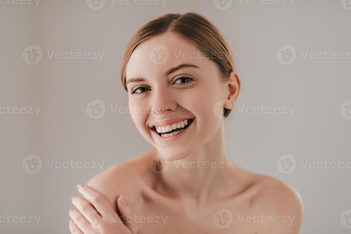 Pure beauty. Portrait of attractive young woman with freckles on face smiling and looking at camera while standing against grey background photo