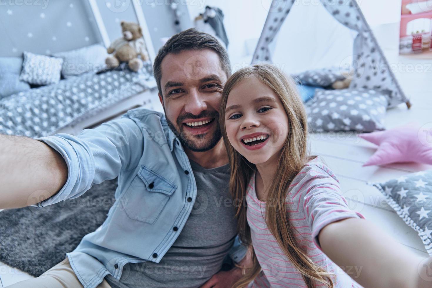 Family is the most important thing. Self portrait of young father and his little daughter smiling while sitting on the floor in bedroom with the tent in the background photo