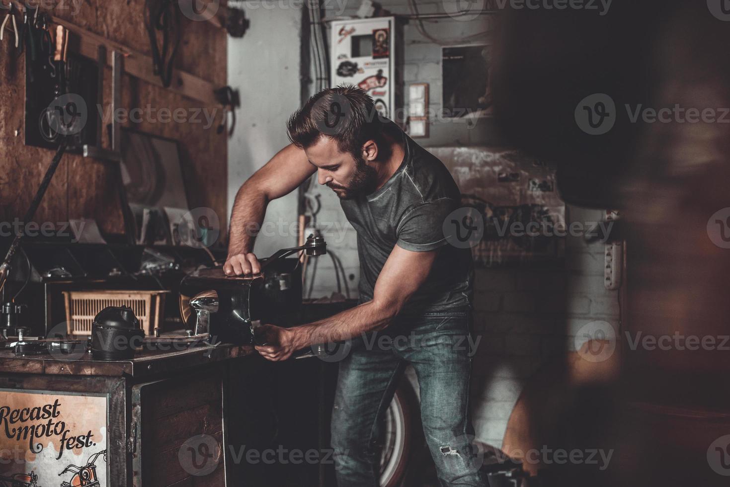 hombre que trabaja en el taller de reparación. joven confiado que usa una herramienta de trabajo mientras trabaja en un taller de reparaciones foto