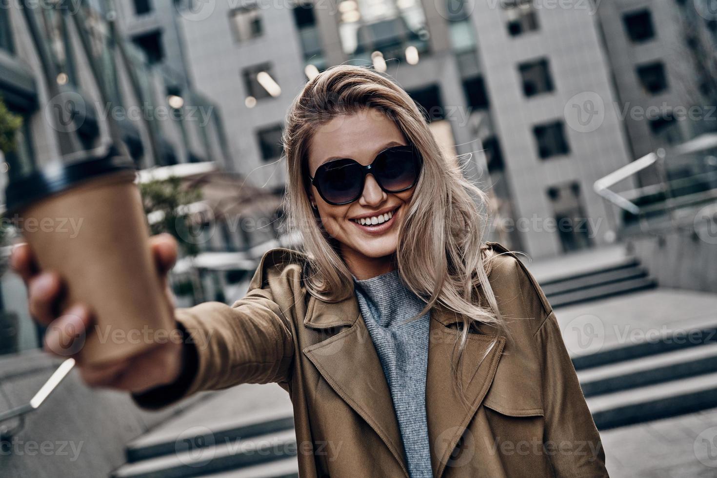 Attractive young woman carrying disposable cup and looking at camera while standing outdoors photo