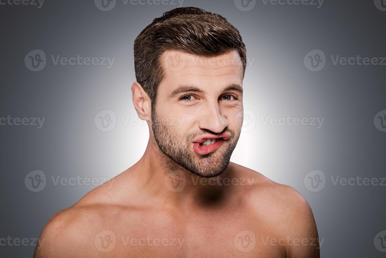 Playful mood. Portrait of handsome young shirtless man looking at camera and grimacing while standing against grey background photo