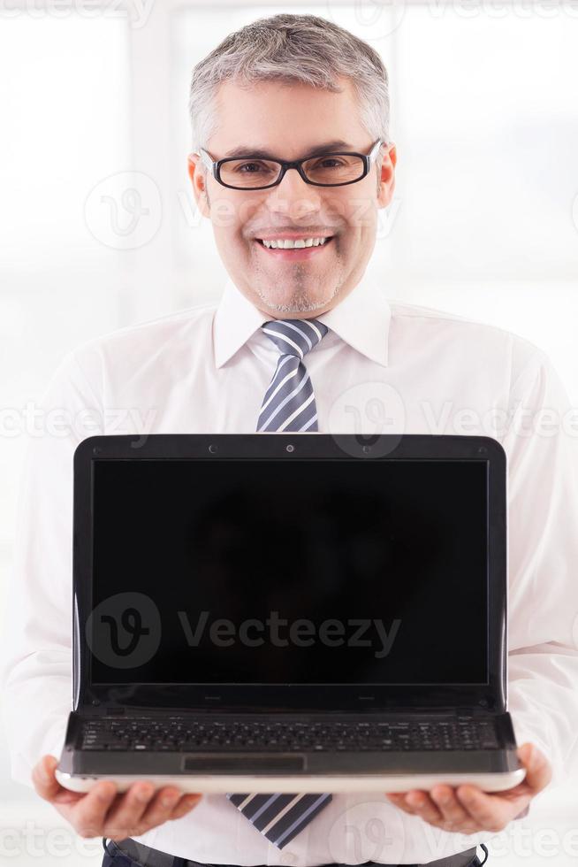 Your advertisement here. Smiling senior man in shirt and tie holding laptop and showing the monitor to you photo