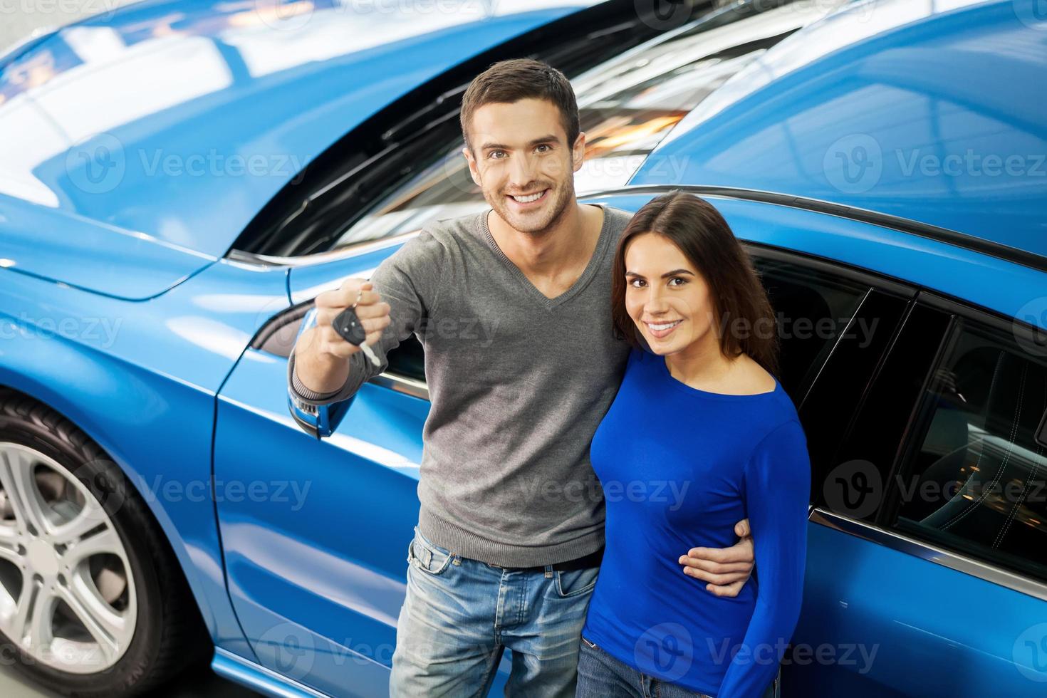 We have made the right choice. Top view of young couple standing near the car at the dealership and holding a key photo