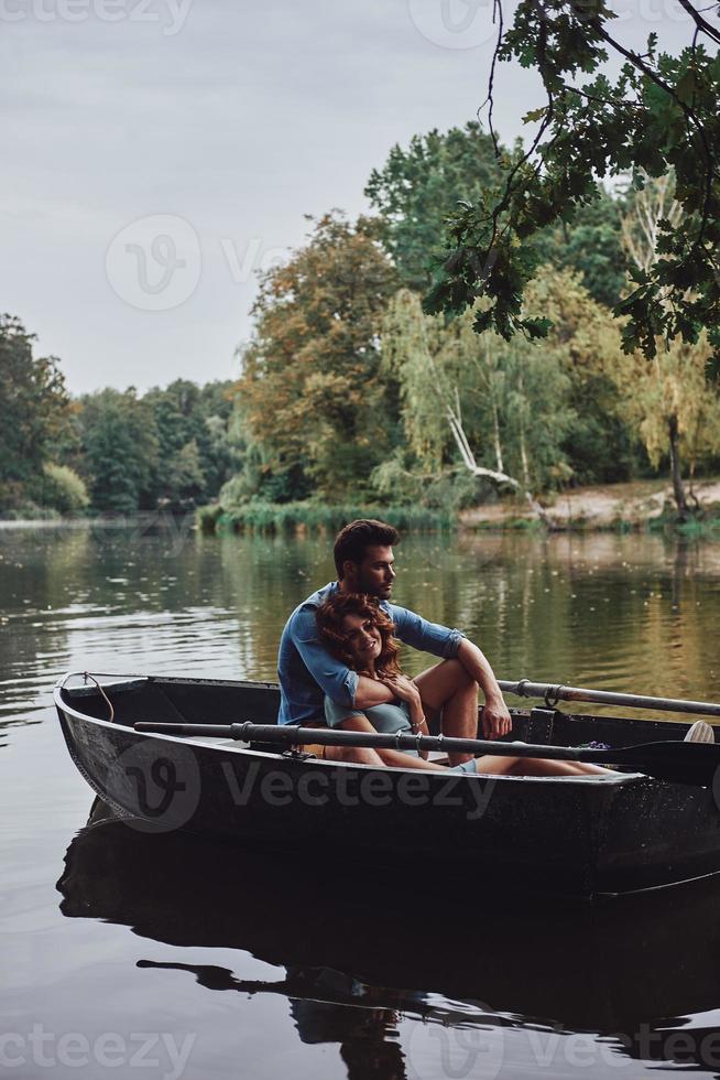 Leaving worries behind. Beautiful young couple embracing and smiling while enjoying romantic date on the lake photo