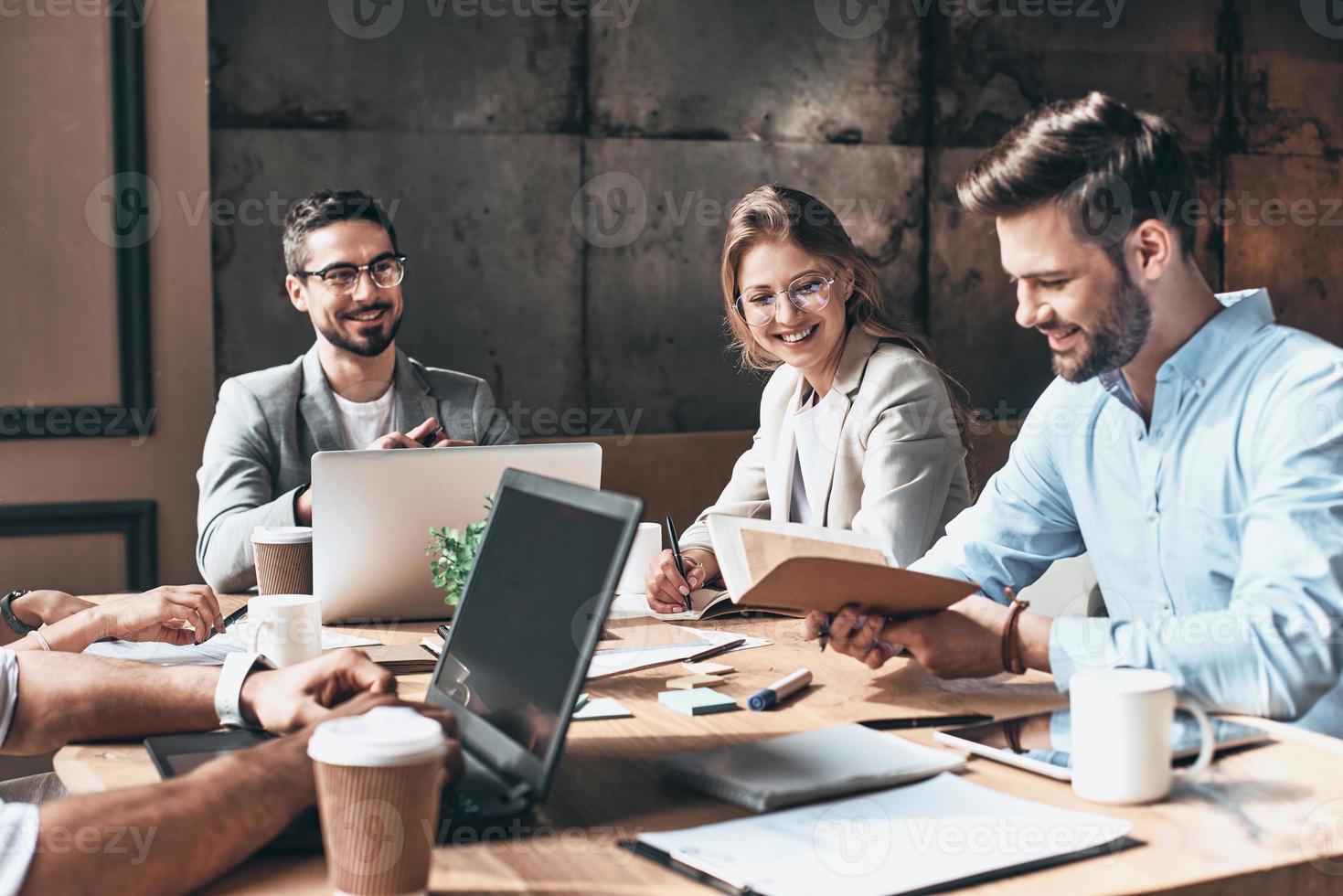 Brainstorming together. Group of young modern people in smart casual wear discussing business and smiling while sitting in the creative office photo