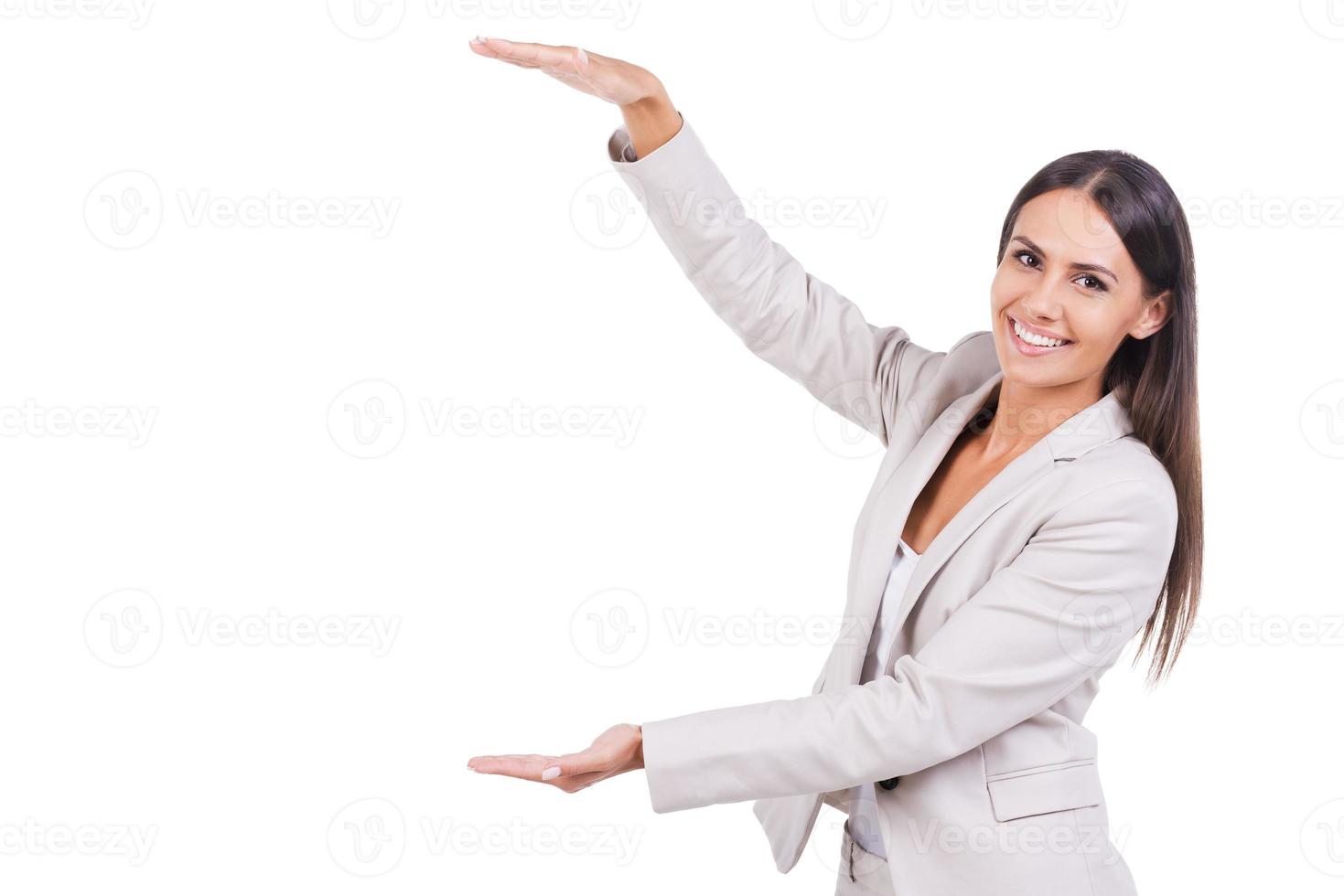 Businesswoman showing size. Beautiful young businesswoman in suit showing large size and smiling while standing against white background photo