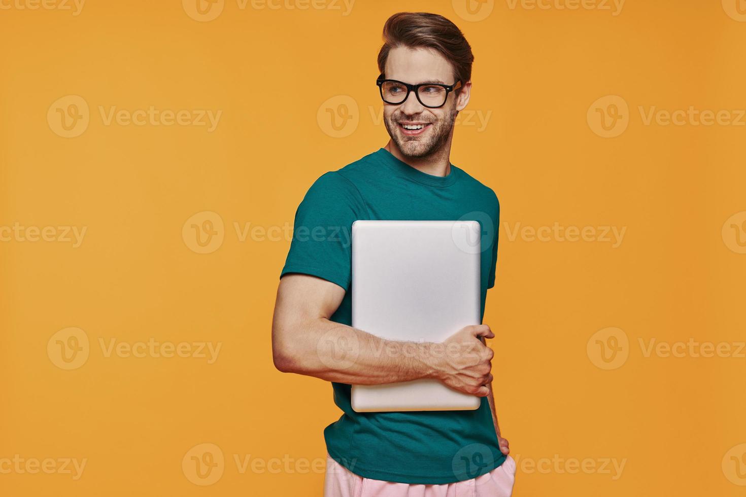 Handsome young man in casual clothing carrying laptop and smiling photo