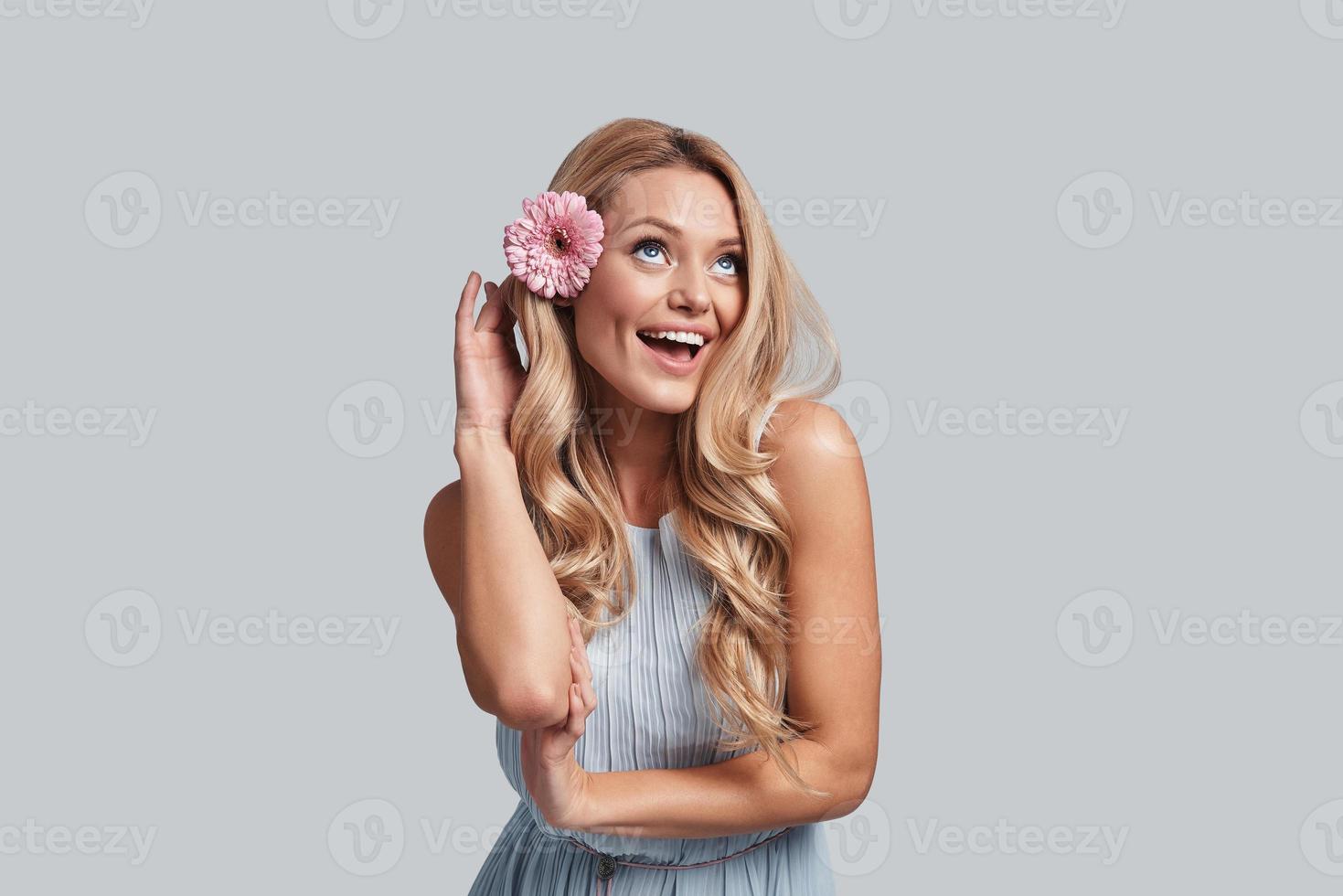 Fresh and cute. Attractive young woman with a flower in hair keeping arms crossed and smiling while standing against grey background photo