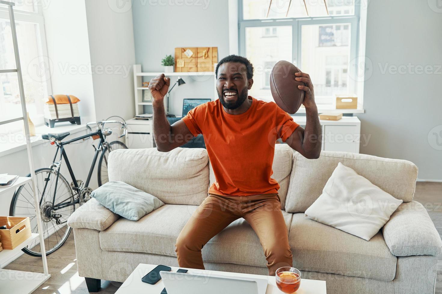Happy young African man cheering and smiling while watching sport match at home photo