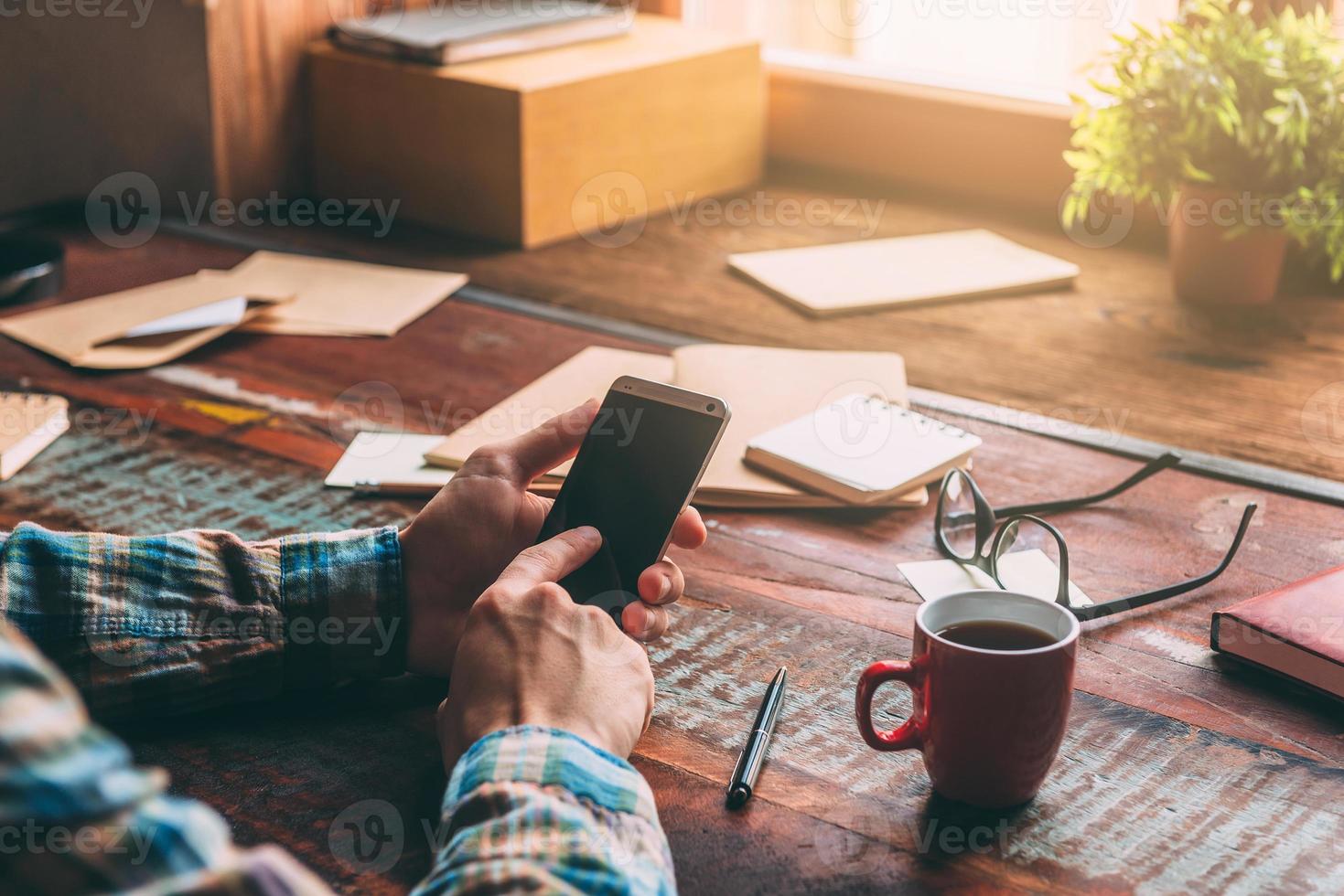 Open for communication. Close-up image of man holding smart phone while sitting at the rustic wooden table photo