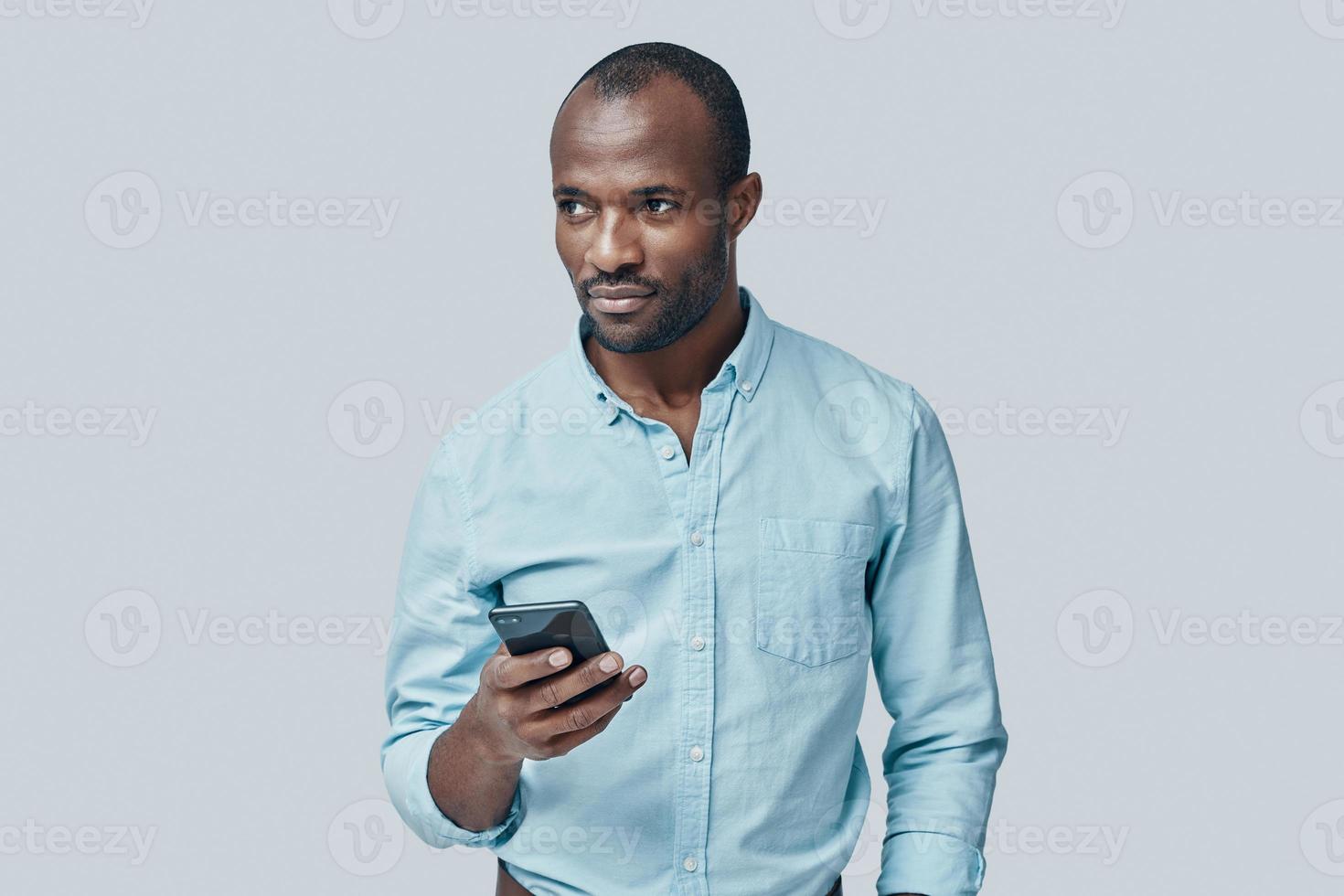 Handsome young African man using smart phone while standing against grey background photo