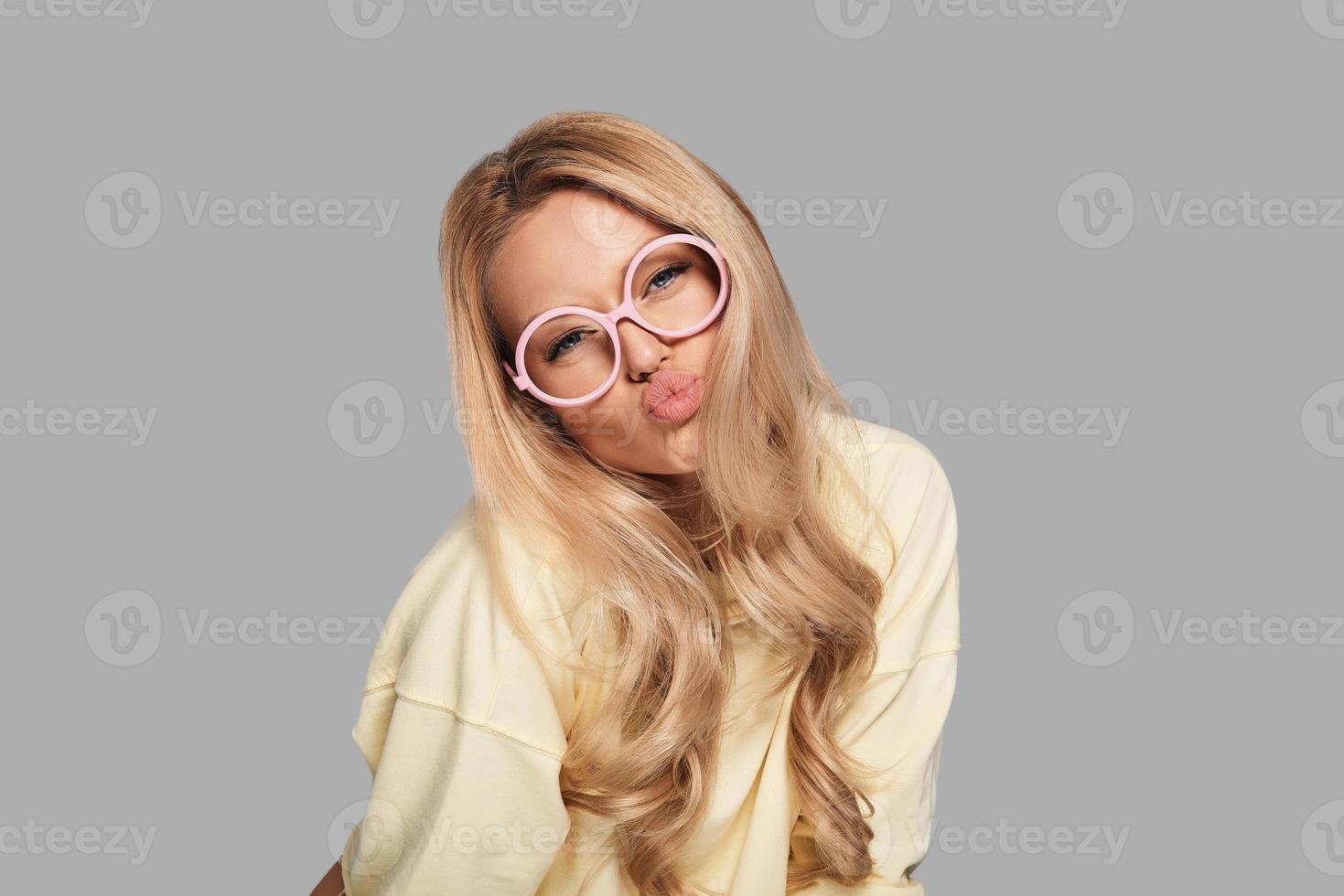 Kissable lips. Beautiful young woman in pink eyewear puckering while standing against grey background photo