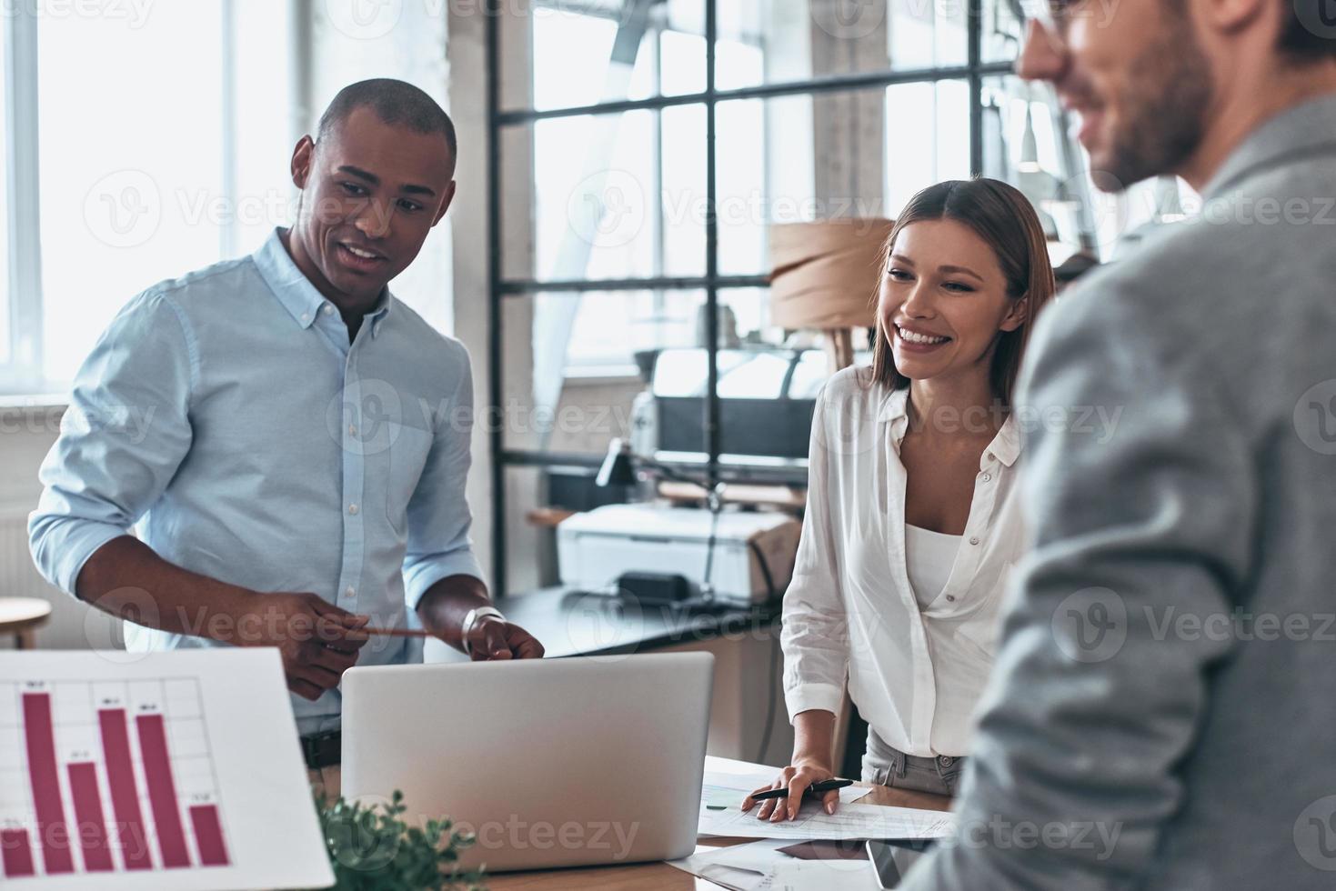 Team working together. Group of young modern people in smart casual wear discussing business while standing in the creative office photo