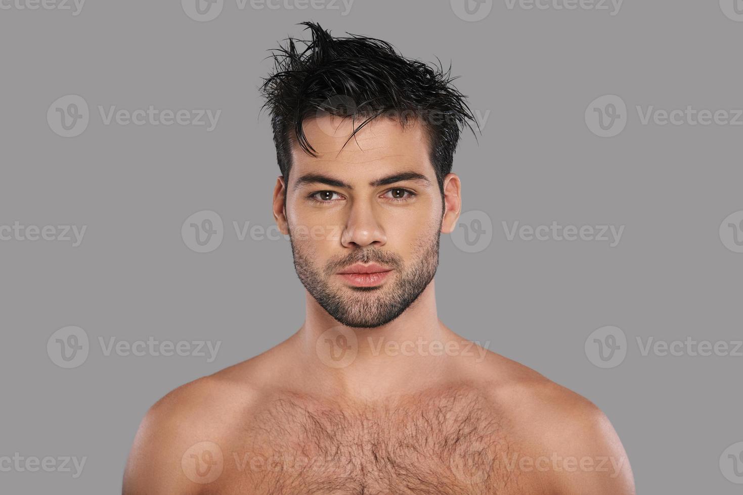 Young and handsome. Good looking young man looking at camera while standing against grey background photo