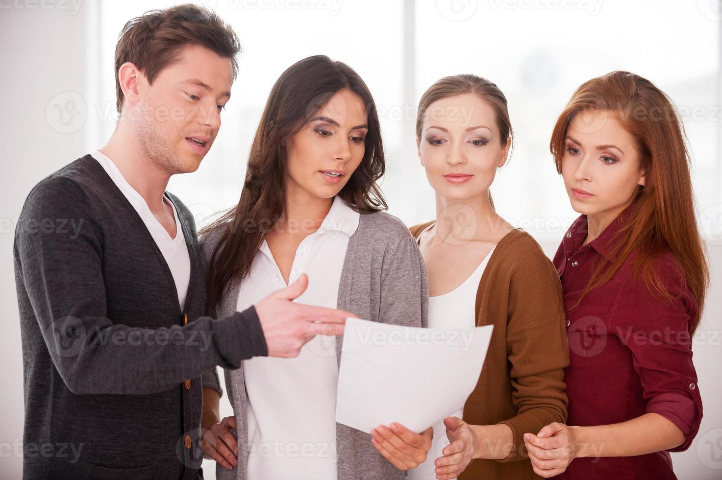 Discussing a contract. Group of young people discussing document while standing close to each other photo