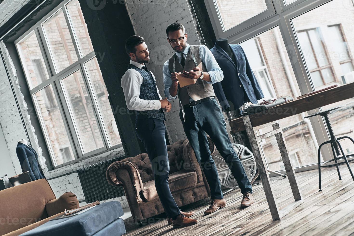 Taking notes. Full length of two young fashionable men having a discussion while standing in workshop photo
