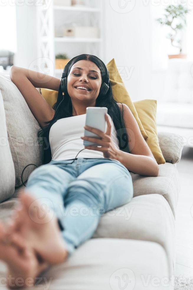 Enjoying music.  Young beautiful woman listening music and smiling while lying on the sofa at home photo