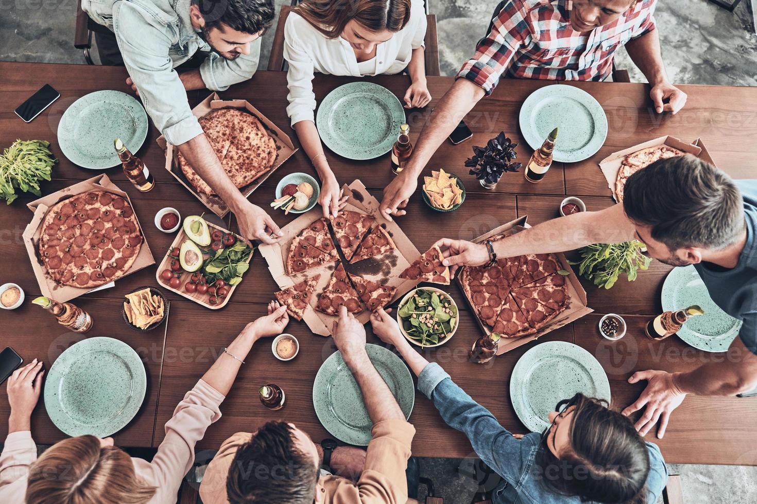 Everything is so delicious. Close up top view of young people picking pizza slices while having a dinner party in indoors photo