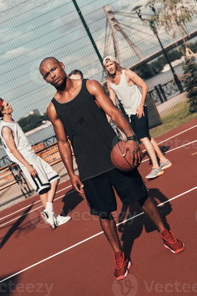 teniendo en cuenta el juego. Longitud total de un joven africano vestido con ropa deportiva mirando hacia otro lado mientras juega al baloncesto al aire libre foto