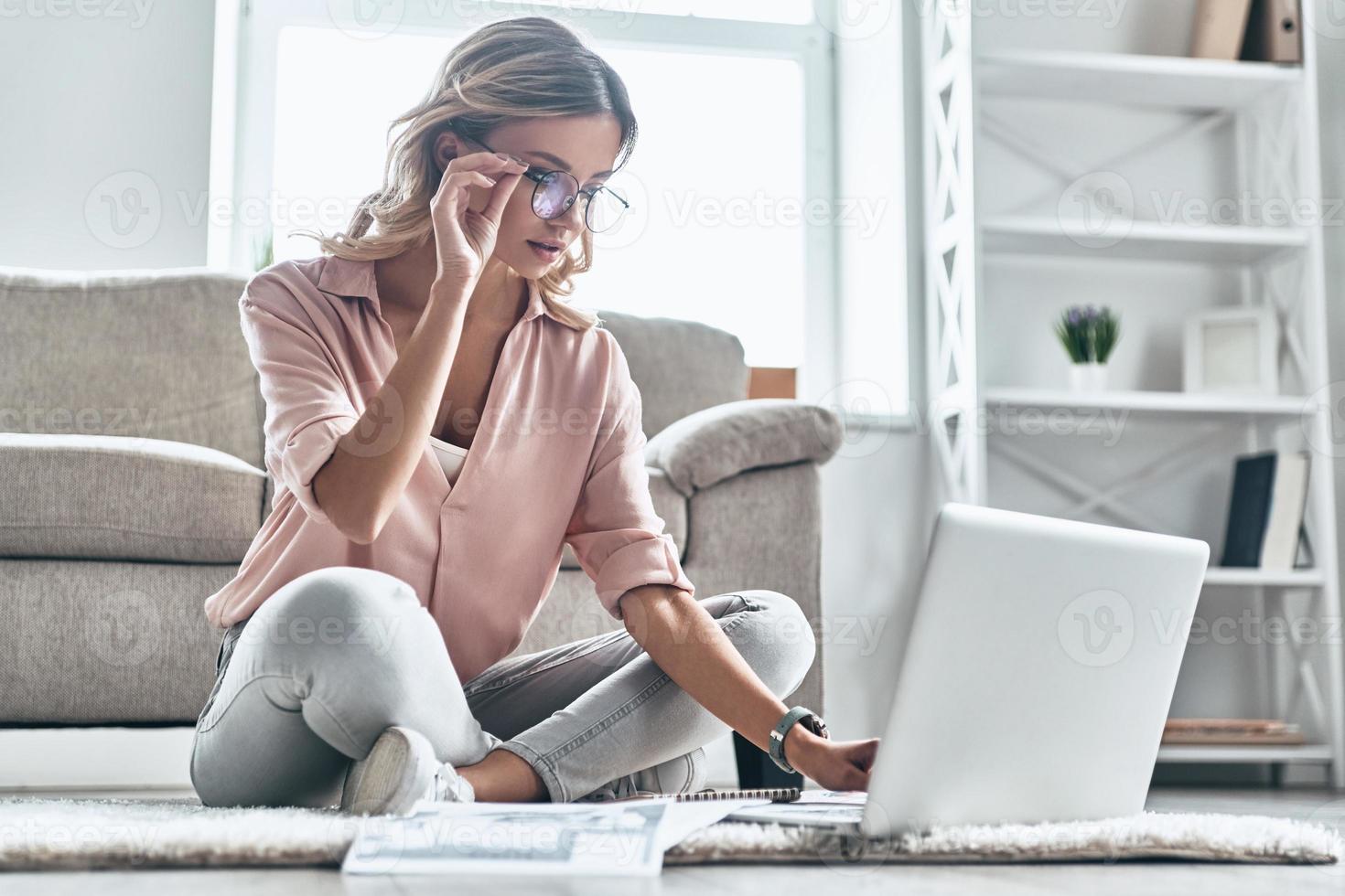 poner ideas en algo real. una joven pensativa con anteojos que trabaja usando una computadora mientras está en el suelo en casa foto