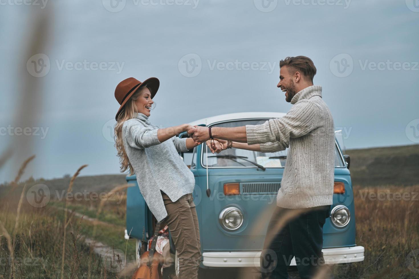 Feeling playful.  Beautiful young couple holding hands and smiling while standing near the blue retro style mini van photo