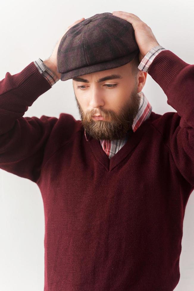 elegante guapo. un joven apuesto con ropa informal tocando su sombrero con la mano y mirando hacia otro lado foto