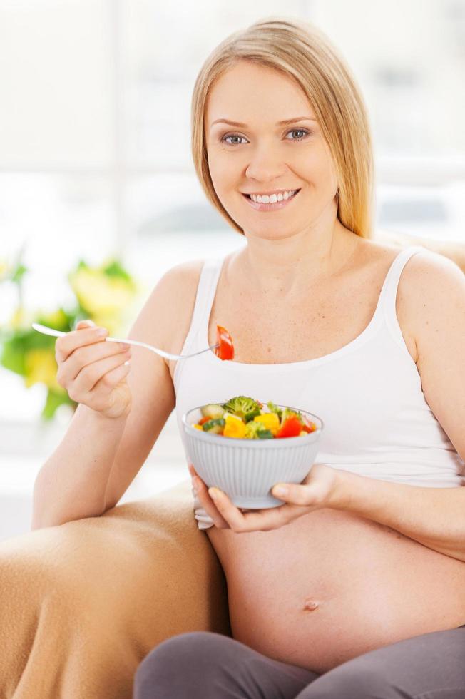 mujer embarazada comiendo ensalada. mujer embarazada feliz sentada en la silla y comiendo ensalada foto